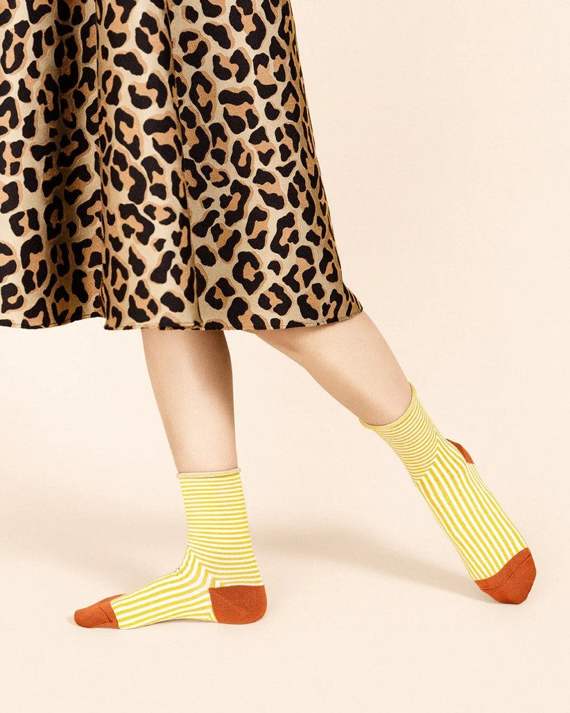 Striped marigold socks with terracotta rust heel and toe at Clad, a sustainable clothing store in Asheville, NC. Paired with a leopard midi skirt.