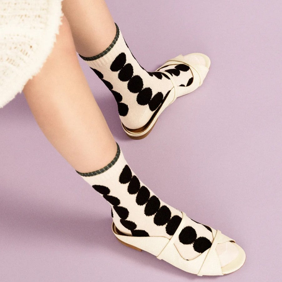 A black polka dot sock with solid white cream background.