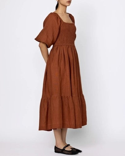 Amber smocked midi linen cotton dress by LAUDE the Label. Puff sleeves, square neckline, and bottom tier. Paired with black flats.