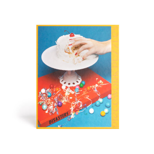 1000 piece colorful puzzle with a hand grabbing cake on top of a book Disasters. Red and blue in color.