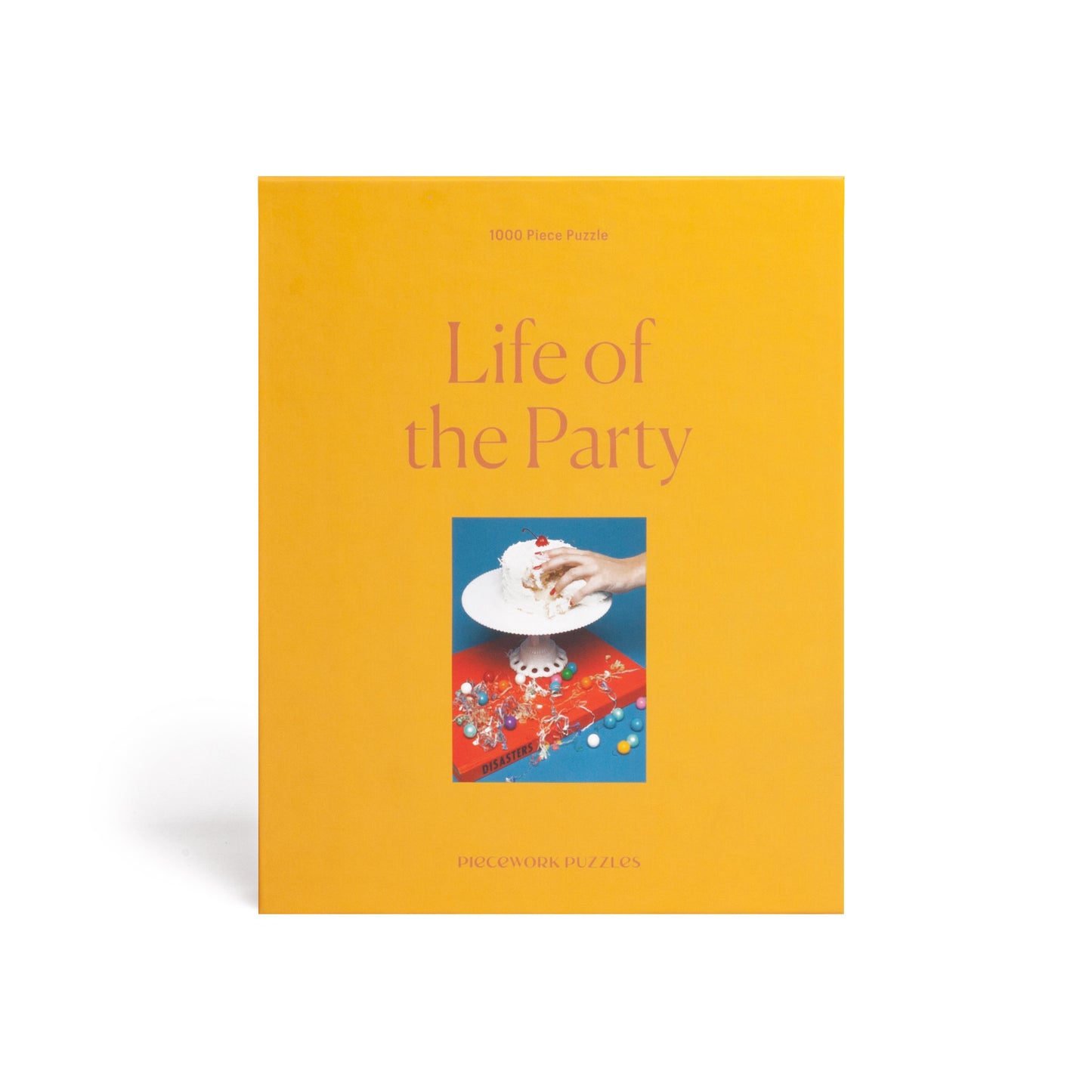 1000 piece colorful puzzle with a hand grabbing cake on top of a book Disasters. Red and blue in color with a yellow box.