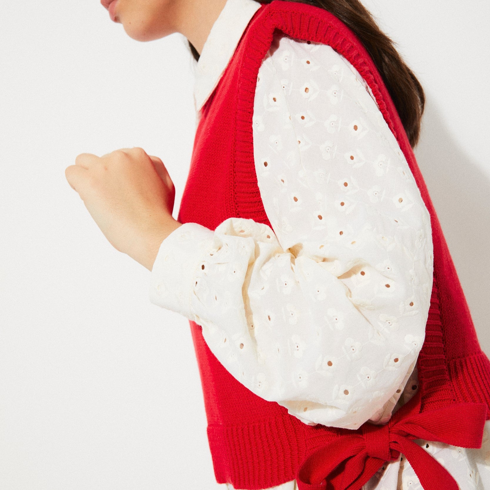 Rita Row red pilea sweater vest with open sides and bow ties on either side at Clad, a sustainable clothing store in Asheville, NC. Paired with a cream eyelet long sleeve blouse.