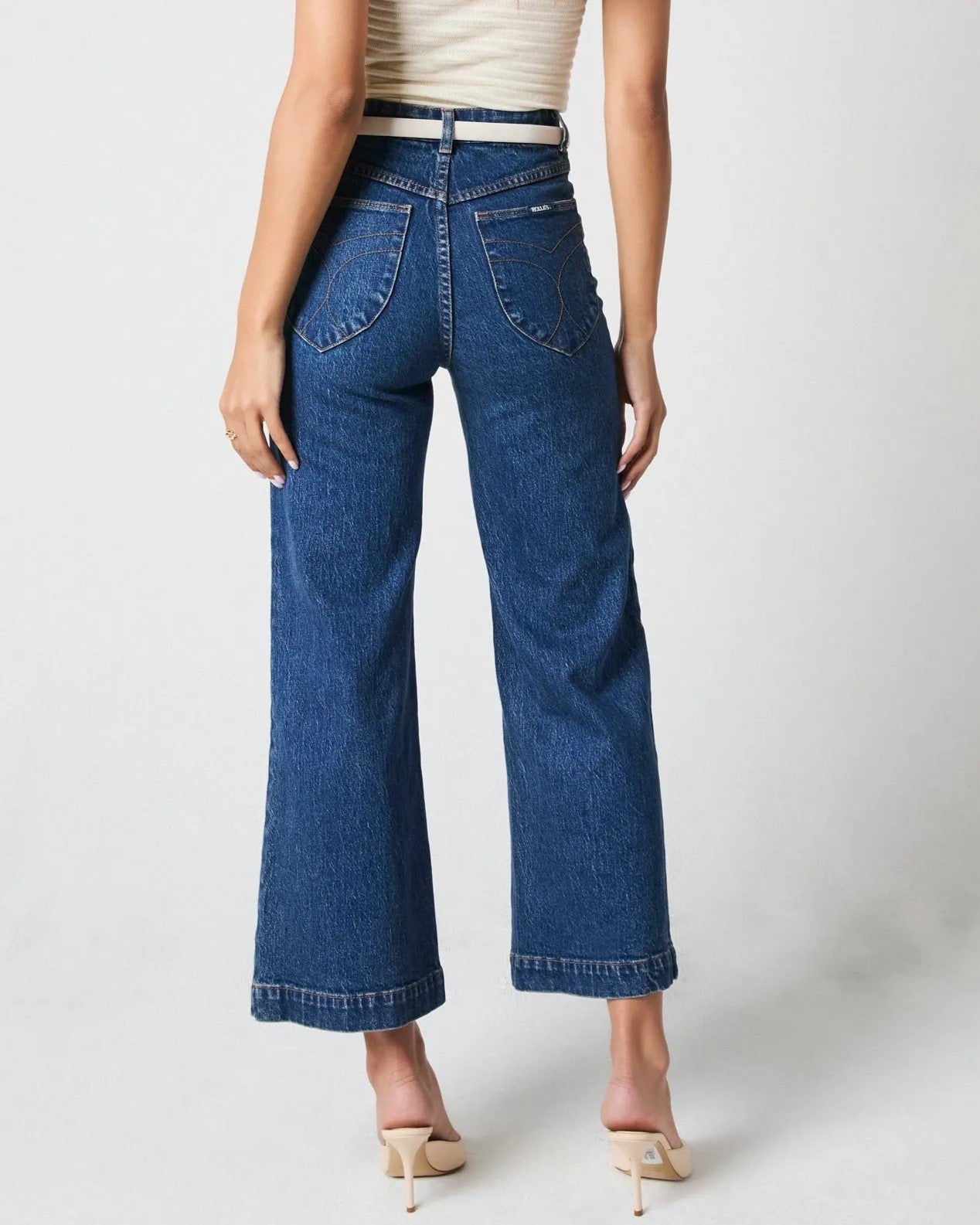 Rolla's sailor jeans with a wide leg in eco ruby dark denim blue. Paired with a white tank top, white leather belt, and beige pump sandals.