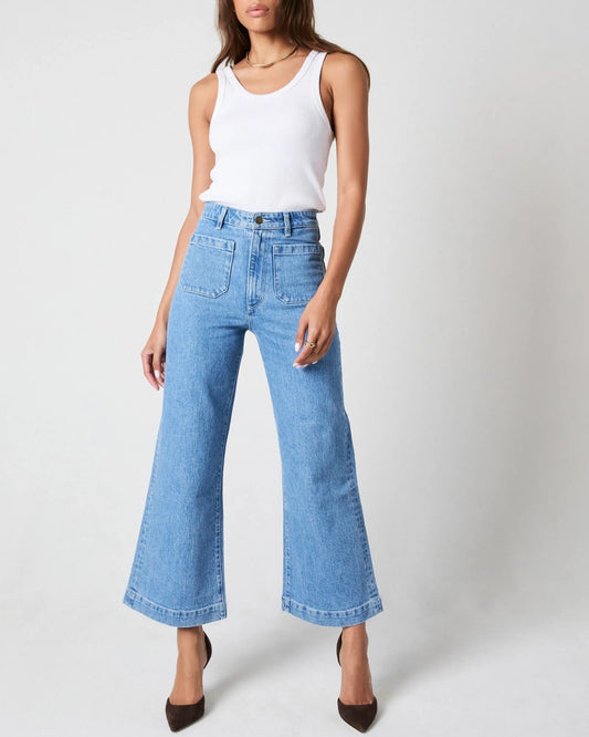 Sailor Jean by Rolla's with ankle crop in lily light mid blue paired with white tank top and black pumps. High-waisted jeans with front pockets.