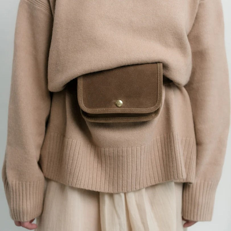 Belt bag by Small Lot Co in brush brown with a metal snap, adjustable waist. Fanny pack style made from cotton canvas. Styled with an oversized sweater.