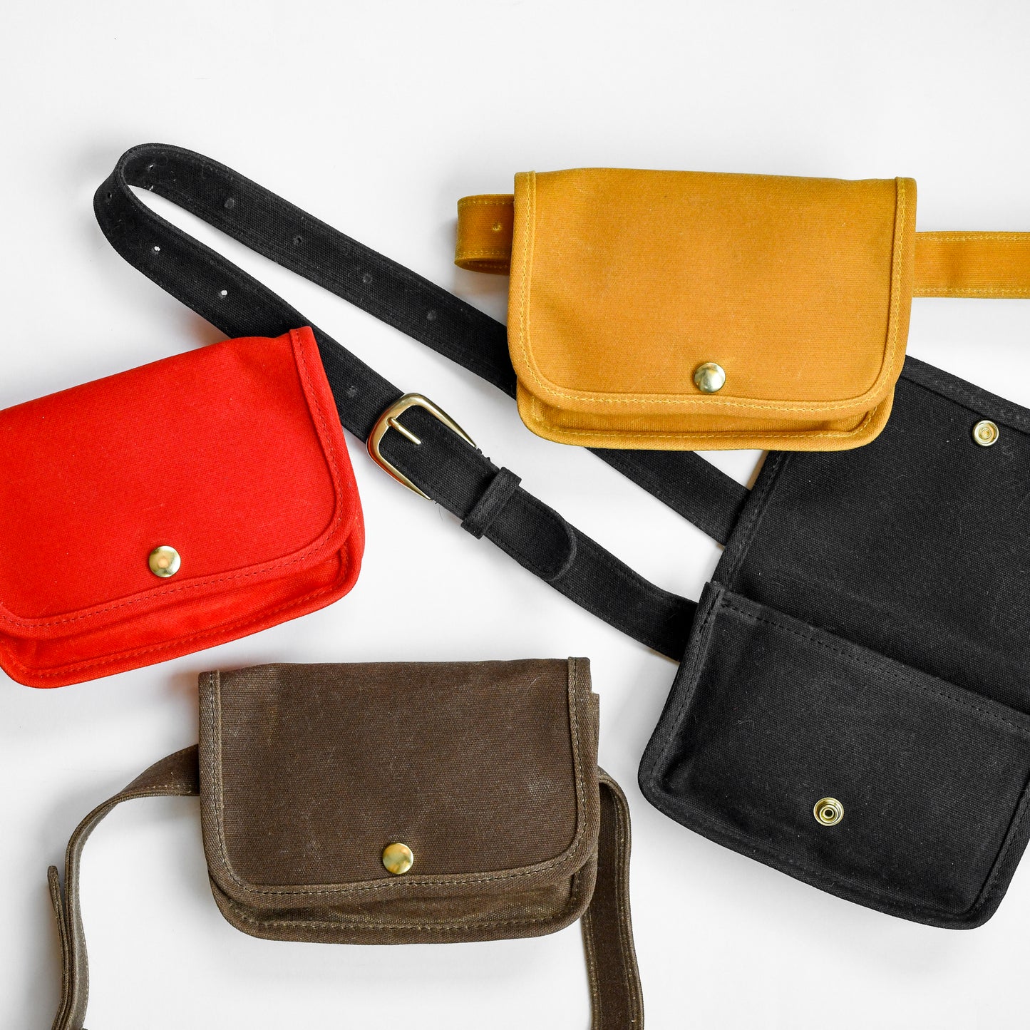 Belt bags by Small Lot Co with a metal snap, adjustable waist. Fanny pack style made from cotton canvas. Red, yellow, black, and brown.