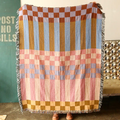 A checkered, reversible tapestry blanket with stripes and fringe.