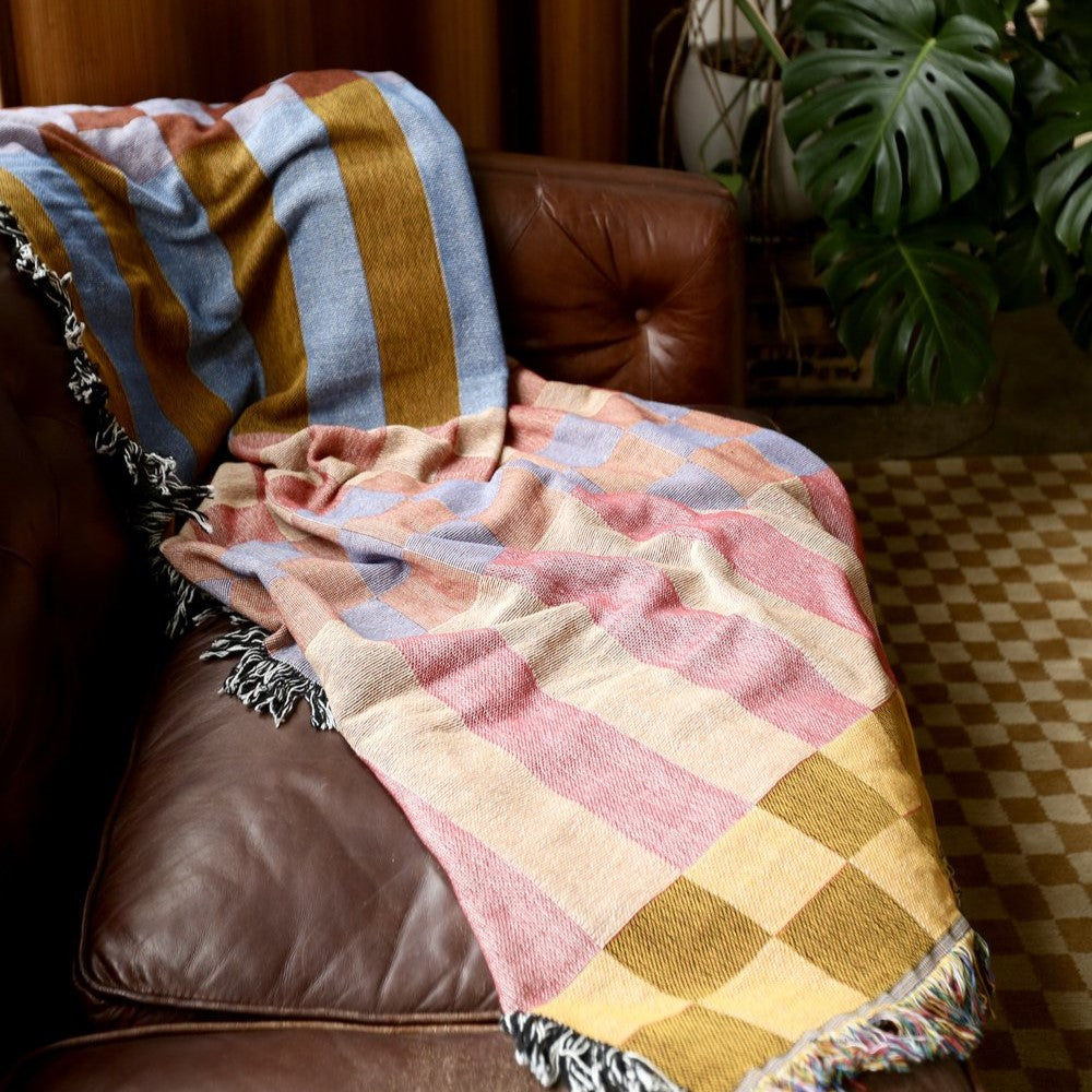 A checkered, reversible tapestry blanket with stripes and fringe.