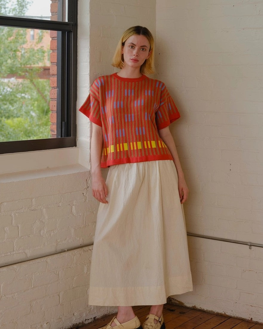 The Endery Bauhaus short sleeve sweater tee in poppy orange with lavender detail, paired with a beige linen midi skirt