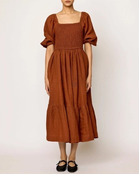 Amber smocked midi linen cotton dress by LAUDE the Label. Puff sleeves, square neckline, and bottom tier. Paired with black flats.