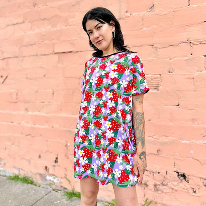 An oversized patterned circle dress with short sleeves and a black hemmed neckline in a berries and floral strawberry print in lilac lavender and red. Made by women-owned brand Nooworks.