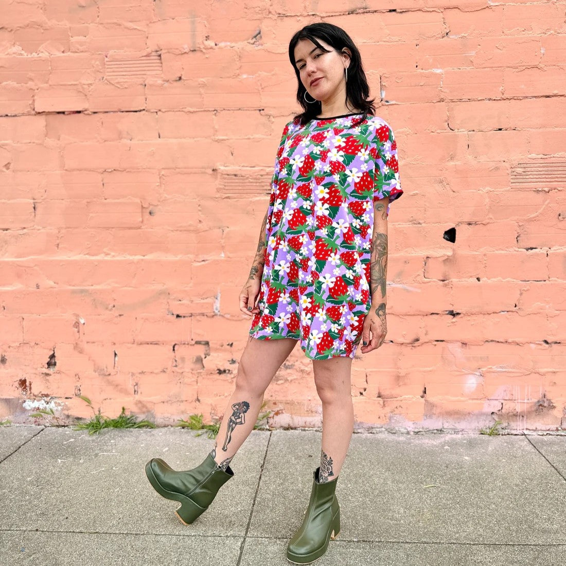 An oversized patterned circle dress with short sleeves and a black hemmed neckline in a berries and floral strawberry print in lilac lavender and red. Made by women-owned brand Nooworks.