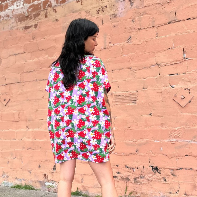 An oversized patterned circle dress with short sleeves and a black hemmed neckline in a berries and floral strawberry print in lilac lavender and red. Made by women-owned brand Nooworks.