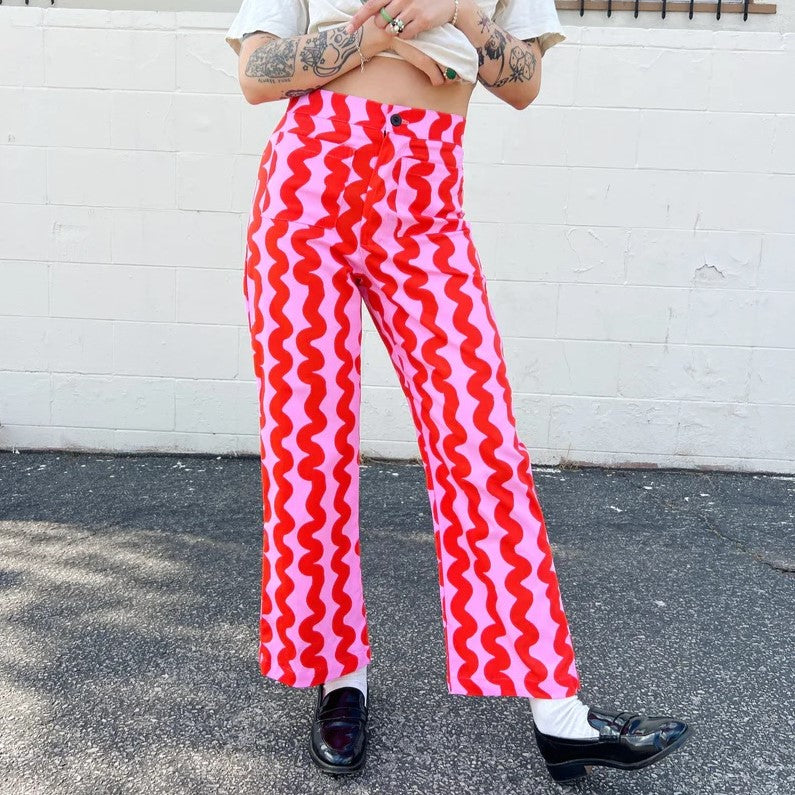 Nooworks pink squiggle casual bell pant with red at Clad, a sustainable clothing store in Asheville, NC. Paired with a destressed white tee and black loafers.