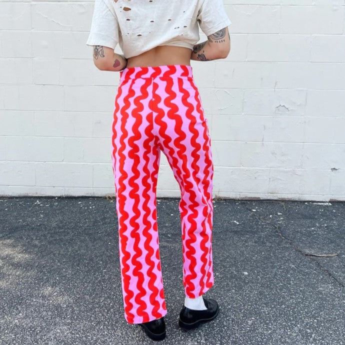 Nooworks pink squiggle casual bell pant with red at Clad, a sustainable clothing store in Asheville, NC. Paired with a destressed white tee and black loafers.