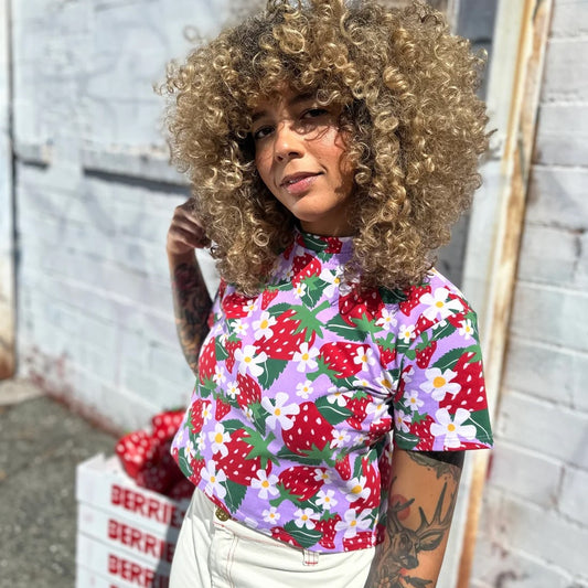 A stretchy berry printed crop top in a strawberry print. Crew neck, lilac lavender background, and yellow and white flowers. Made in California by women-owned business Nooworks.