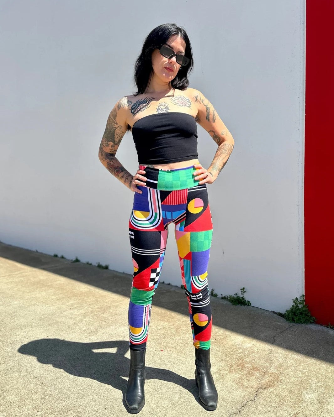 Leggings in Noowork's new print Ansley with bold, abstract shapes and colors yellow, green, red, blue, pink, and black. High waist and paired with a black tube top and boots.