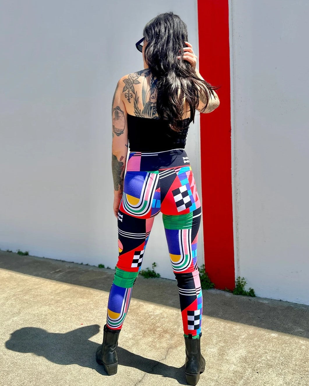 Leggings in Noowork's new print Ansley with bold, abstract shapes and colors yellow, green, red, blue, pink, and black. High waist and paired with a black tube top and boots.