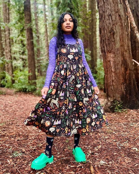 Nooworks Linen Tarot Garden Naomi Dress. Tank top with a midi pleated skirt. Layered over a purple mesh turtleneck with chunky aqua clogs and black socks.