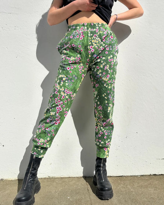 A green floral jogger pant with flowers and an elastic waistband. Made in California by women-owned business Nooworks. Paired with black boots.