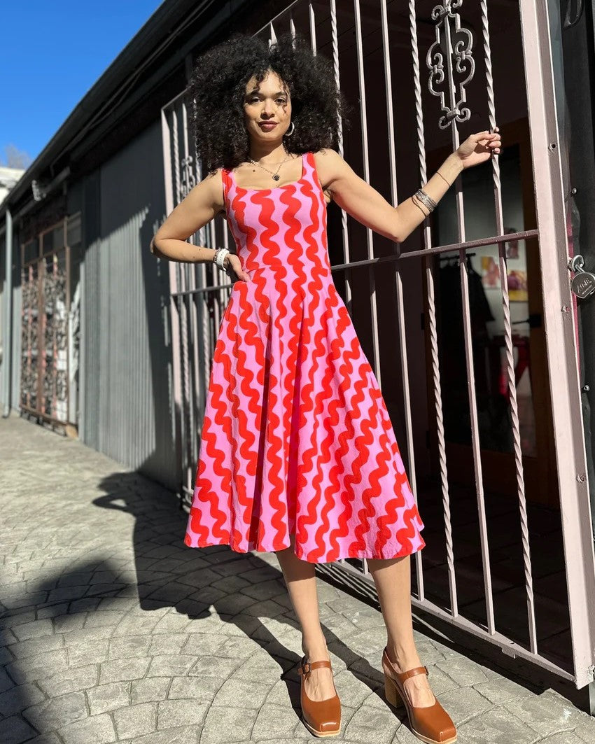 Pink Squiggle Vacation Dress by Nooworks at Clad, a sustainable clothing store in Asheville, NC. Scoop neck with thick straps and a midi skirt. Paired with clogs.