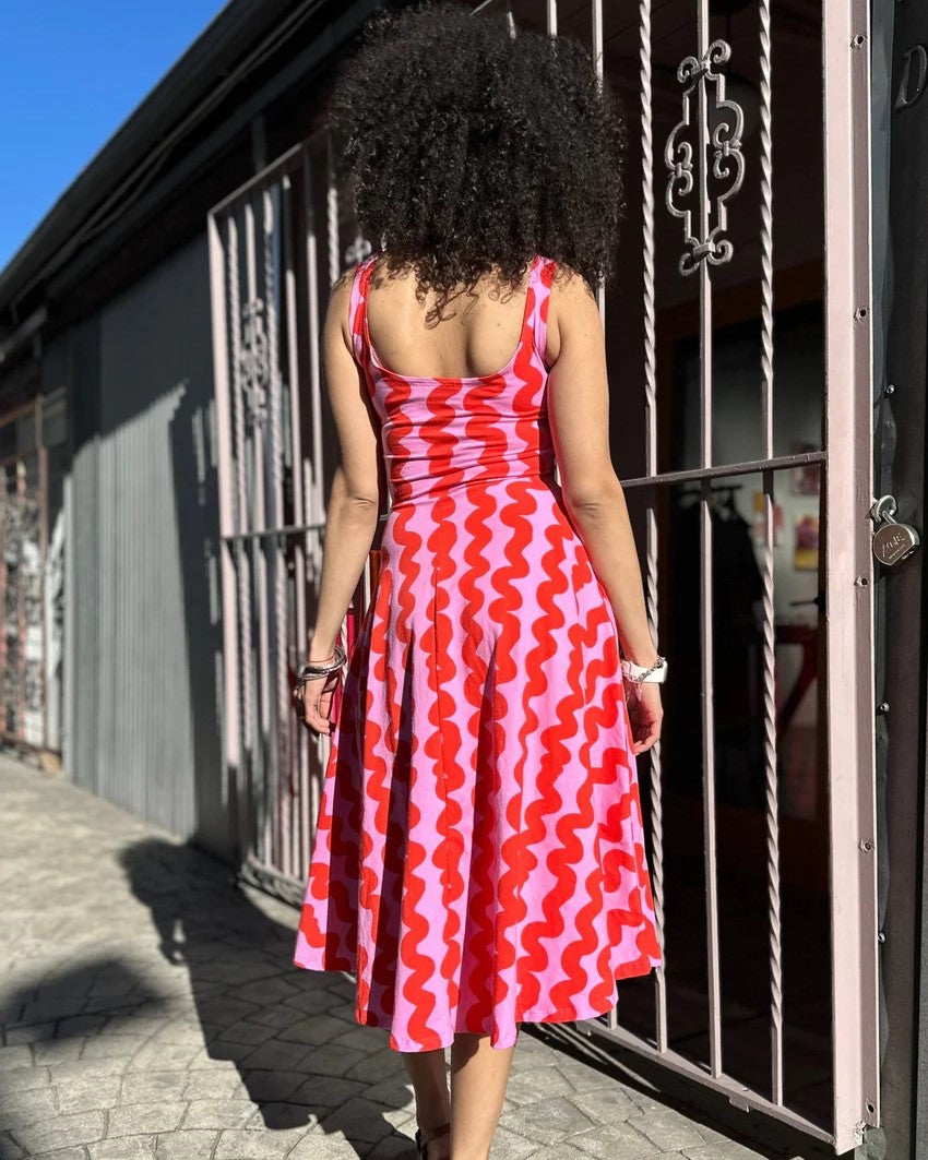 Pink Squiggle Vacation Dress by Nooworks at Clad, a sustainable clothing store in Asheville, NC. Scoop neck with thick straps and a midi skirt. Paired with clogs.