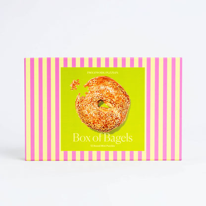 A pink and yellow striped box with 12 small 45-piece puzzles of various bagels.