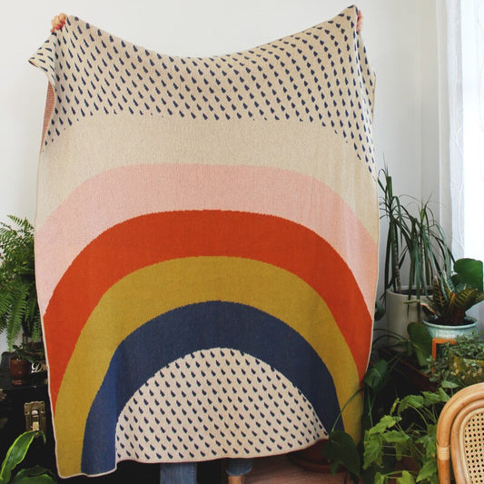 A cotton throw blanket with a colorful rainbow and patterned raindrops.