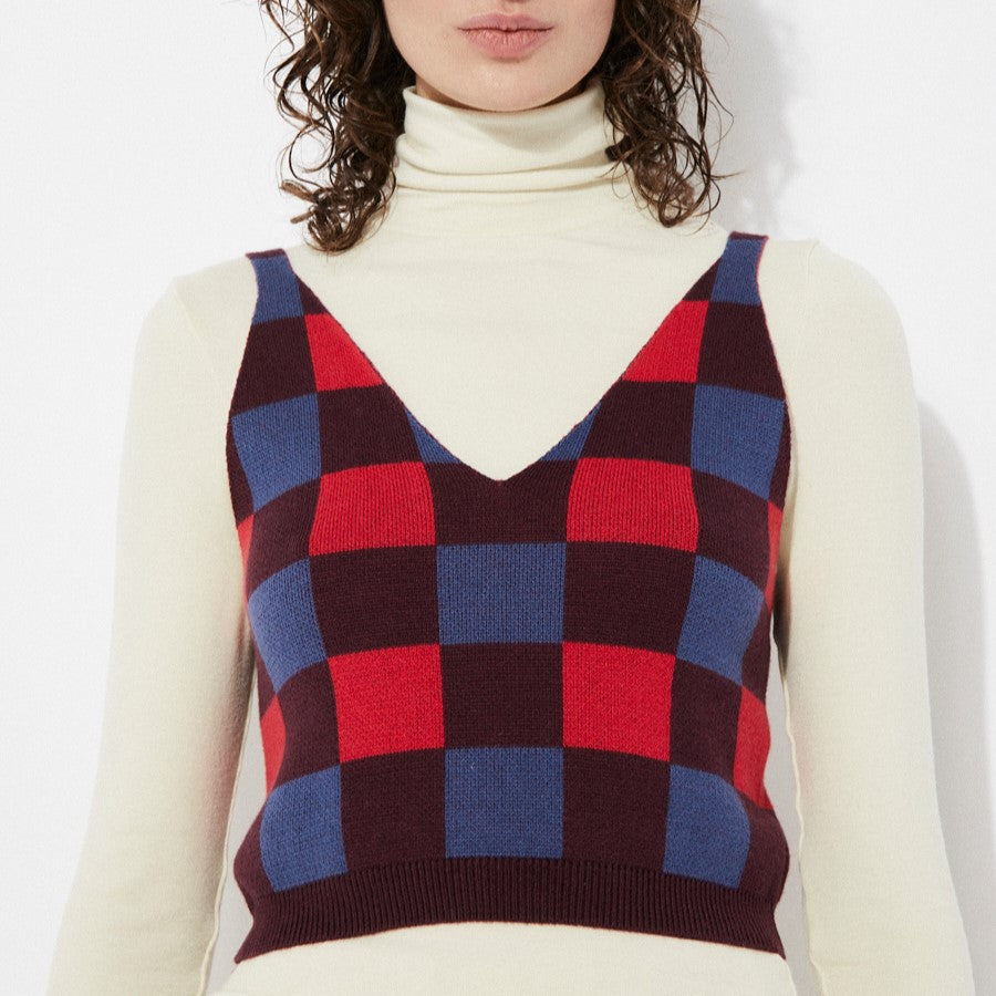 Sleeveless checkered sweater tank in burgundy, blue, and poppy red. V-neck with thick straps layered over a fittered cream turtleneck. Made by Rita Row in Spain.