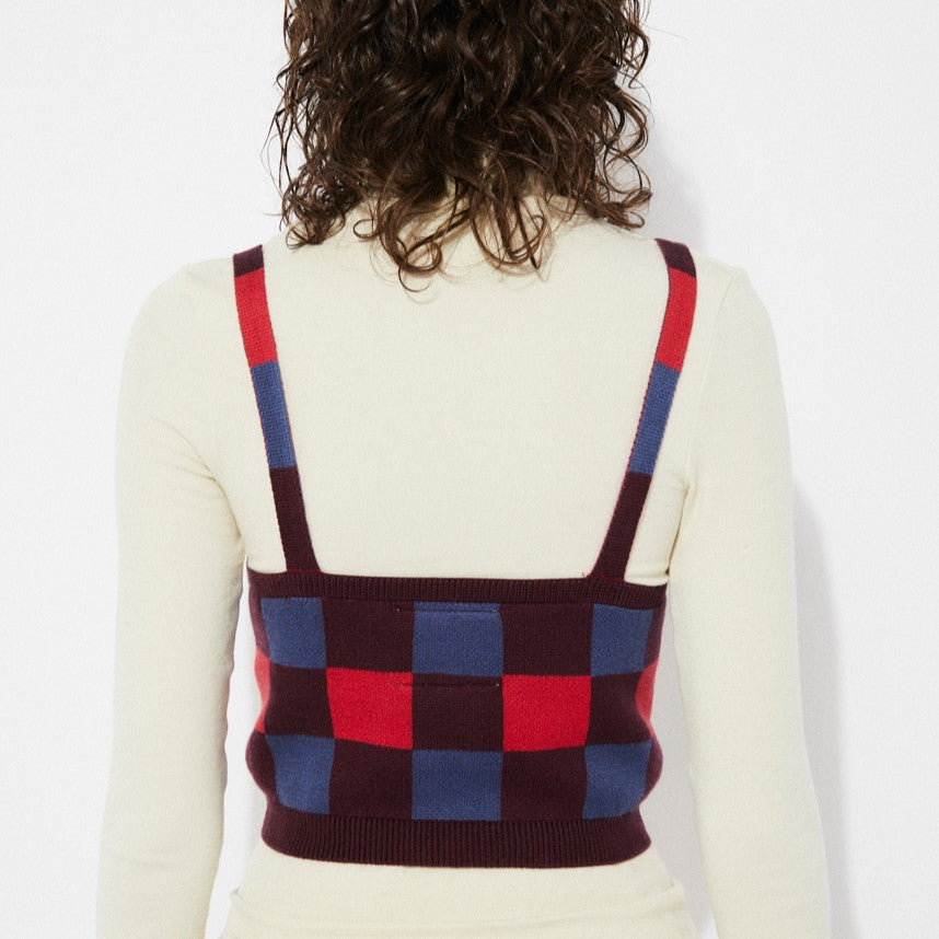 Sleeveless checkered sweater tank in burgundy, blue, and poppy red. V-neck with thick straps layered over a fittered cream turtleneck. Made by Rita Row in Spain.