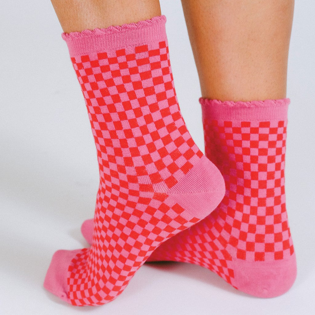 A pink and red checker print sock with scalloped hem.