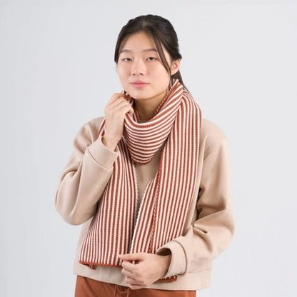 Rust and white pinstripe knit scarf made of upcycled deadstock acrylic yarn by Verloop. Paired with a beige sweatshirts and brick rust drawstring pants.